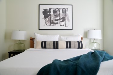 Modern bedroom with matching glass lamps, blue blanket, striped bolster pillow, black and white art.